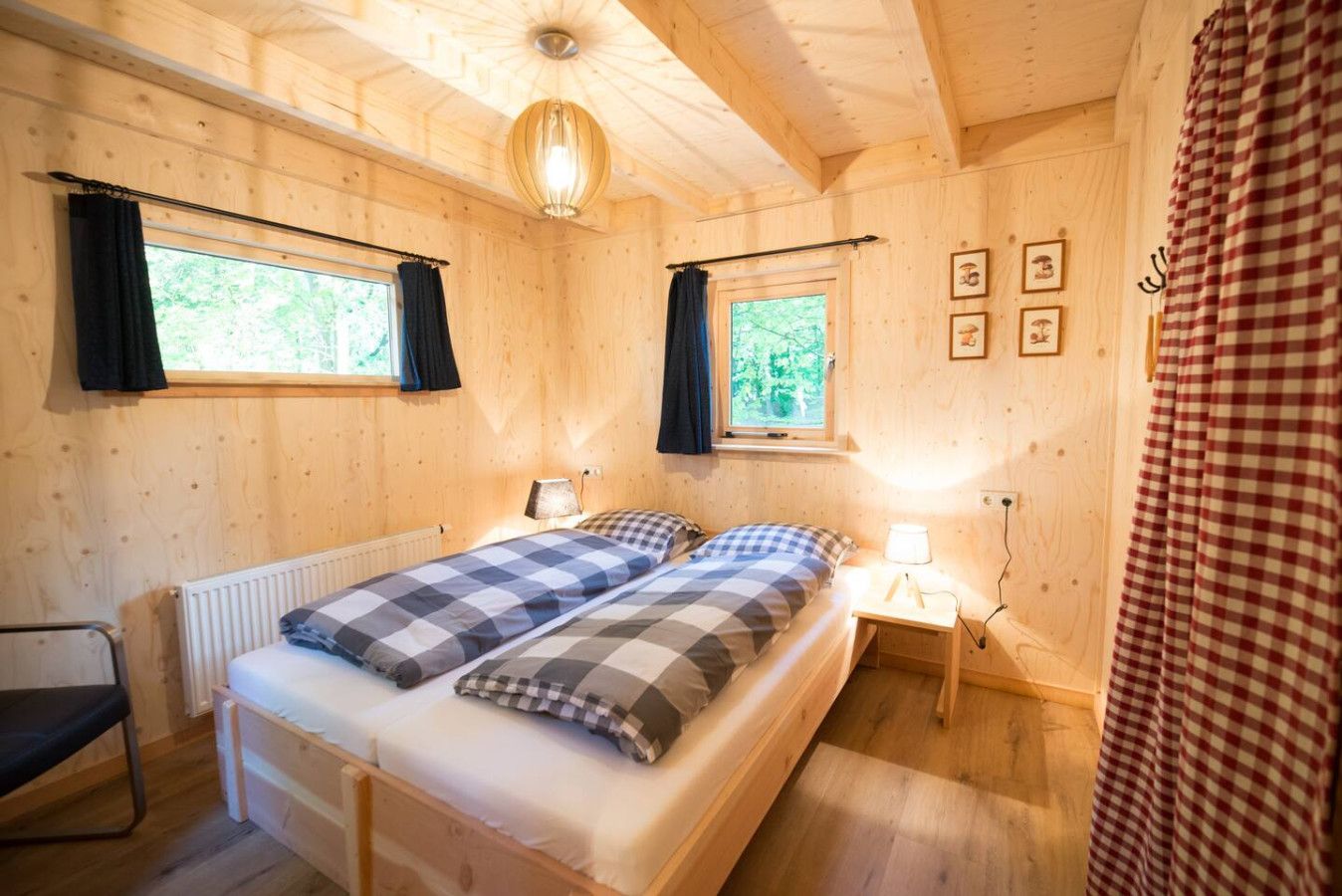 Een houten slaapkamer met een bed, twee nachtkastjes, een radiator en een raam met gordijnen.