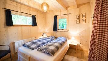 Een houten slaapkamer met een bed, twee nachtkastjes, een radiator en een raam met gordijnen.