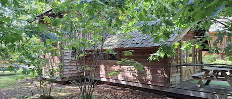 A wooden cabin with a porch, surrounded by trees and a picnic table.