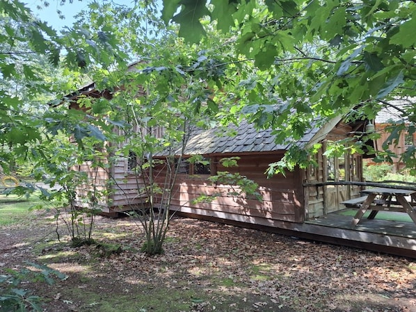 A wooden cabin with a porch, surrounded by trees and a picnic table.