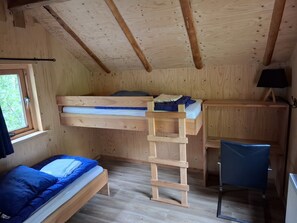 A wooden cabin with bunk beds, a ladder, a desk, and a chair.