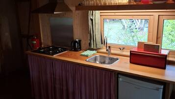 Une cuisine compacte dotée d’un plan de travail en bois, d’un évier, d’un lave-vaisselle et d’une fenêtre donnant sur un espace verdoyant.