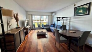 A modern living room with a sofa, coffee table, and dining table. There is a TV on a stand, a plant, and a window with a view of the outside. - NEW! "Le Débarcadère" 4P near Palais Congrès (Paris)