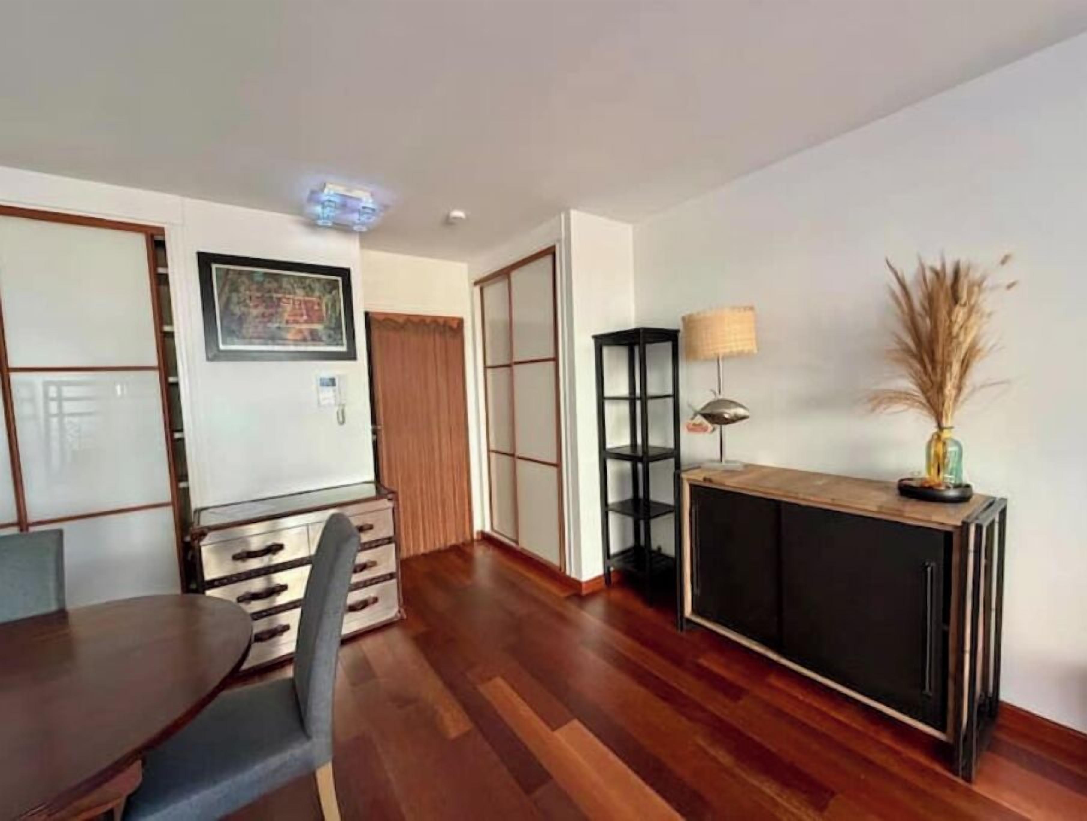 Una sala de estar moderna con piso de madera, una mesa de comedor con sillas, una consola negra con una lámpara y un armario con puertas corredizas.