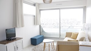 Ein modernes Wohnzimmer mit großem Fenster, einer Couch, einem Couchtisch, einem Fernseher auf einem Schrank und einer blauen Bank.