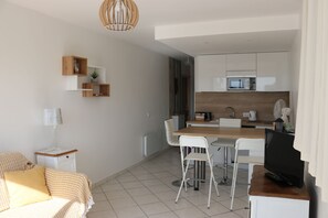 A modern kitchen with white cabinets, a microwave, and a dining area with a table and chairs. - Studio with harbour view, close to the beach - Carnon ideal for short stays (Mauguio)