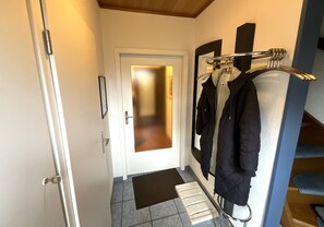 Ein Flur mit einer zurueckfuehrenden Tür, einem Garderobenständer mit Jacken und einer kleinen Stufe, die zum Raum fuehrt.
