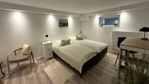 Quarto com cama, mesa de cabeceira, cadeira, escrivaninha e janela com vista.