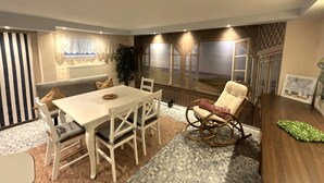 Uma sala de estar moderna com uma mesa de jantar, cadeiras brancas, uma poltrona de balanço e uma janela grande com vista.