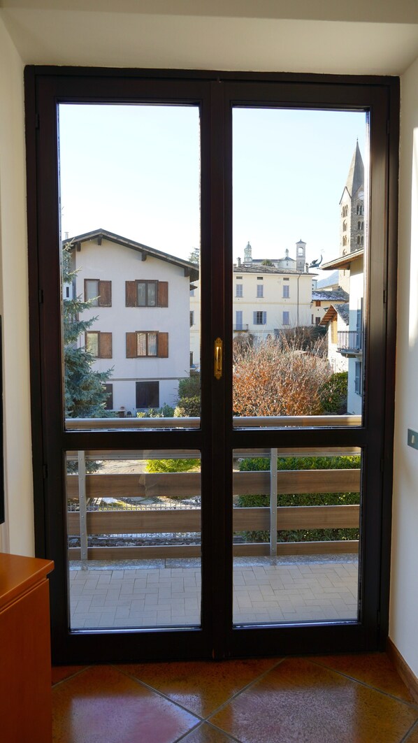 A double door with a view of a building with multiple windows and a bell tower.