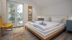 Une chambre moderne avec un grand lit, un fauteuil jaune et une vue à travers la porte vitrée.