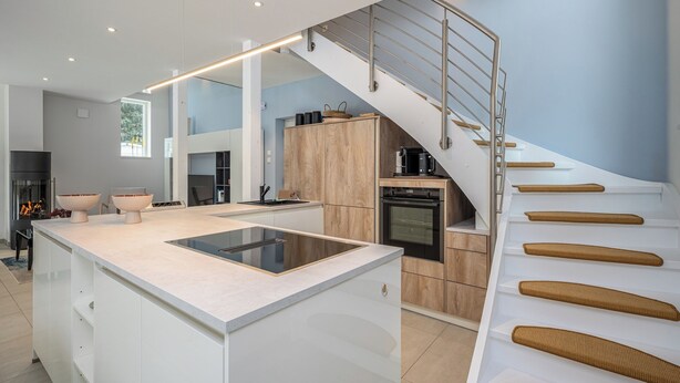 Une cuisine moderne dotée d’un îlot central, d’un four encastré et d’un escalier avec des marches en bois.