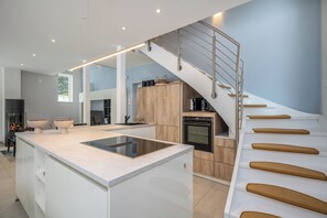 Una cocina moderna con una isla central, horno empotrado y una escalera con escalones de madera.