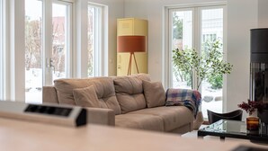 Un salon moderne avec un canapé beige, un meuble jaune et une grande fenêtre donnant sur un paysage enneigé.