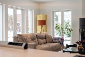 A modern living room with a beige sofa, a yellow cabinet, and a large window with a view of a snowy landscape. - Comfortable vacation home for time for two (Dierhagen)