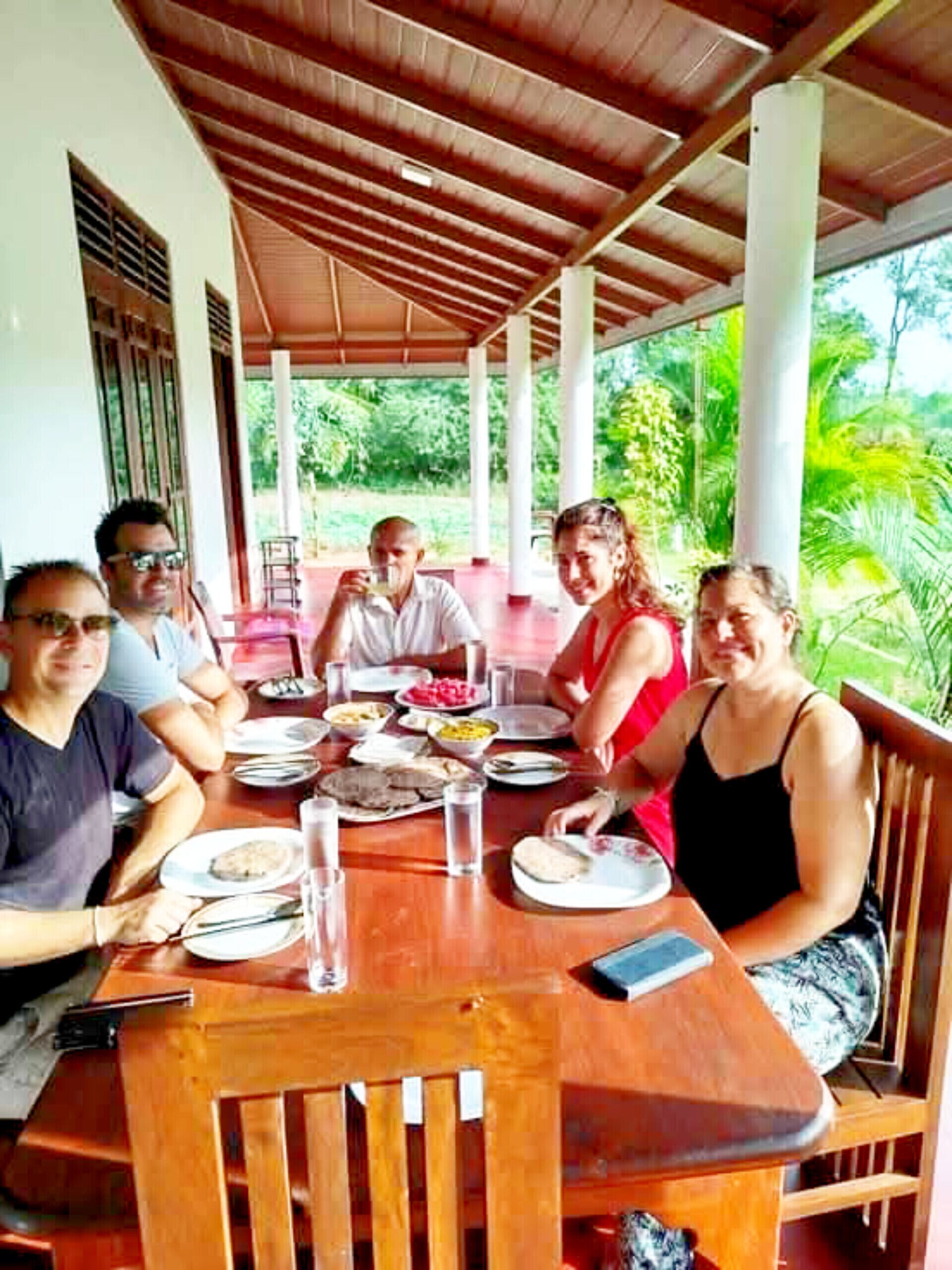 Un groupe de personnes est assis à une table en bois, à l'extérieur, et profite de la vue sur la verdure environnante.