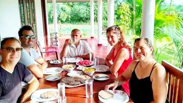 Un groupe de personnes est assis à une table en bois, à l'extérieur, et profite de la vue sur la verdure environnante.