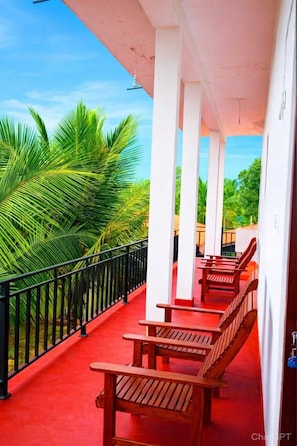 A covered outdoor seating area with wooden benches and a red floor, surrounded by a black railing and palm trees. - Wilpattu Gagana Guest  (Pahala Maragahawewa)