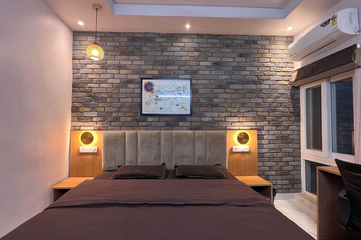 A bedroom with a brick wall, a bed with a headboard, two bedside tables, and a window.
