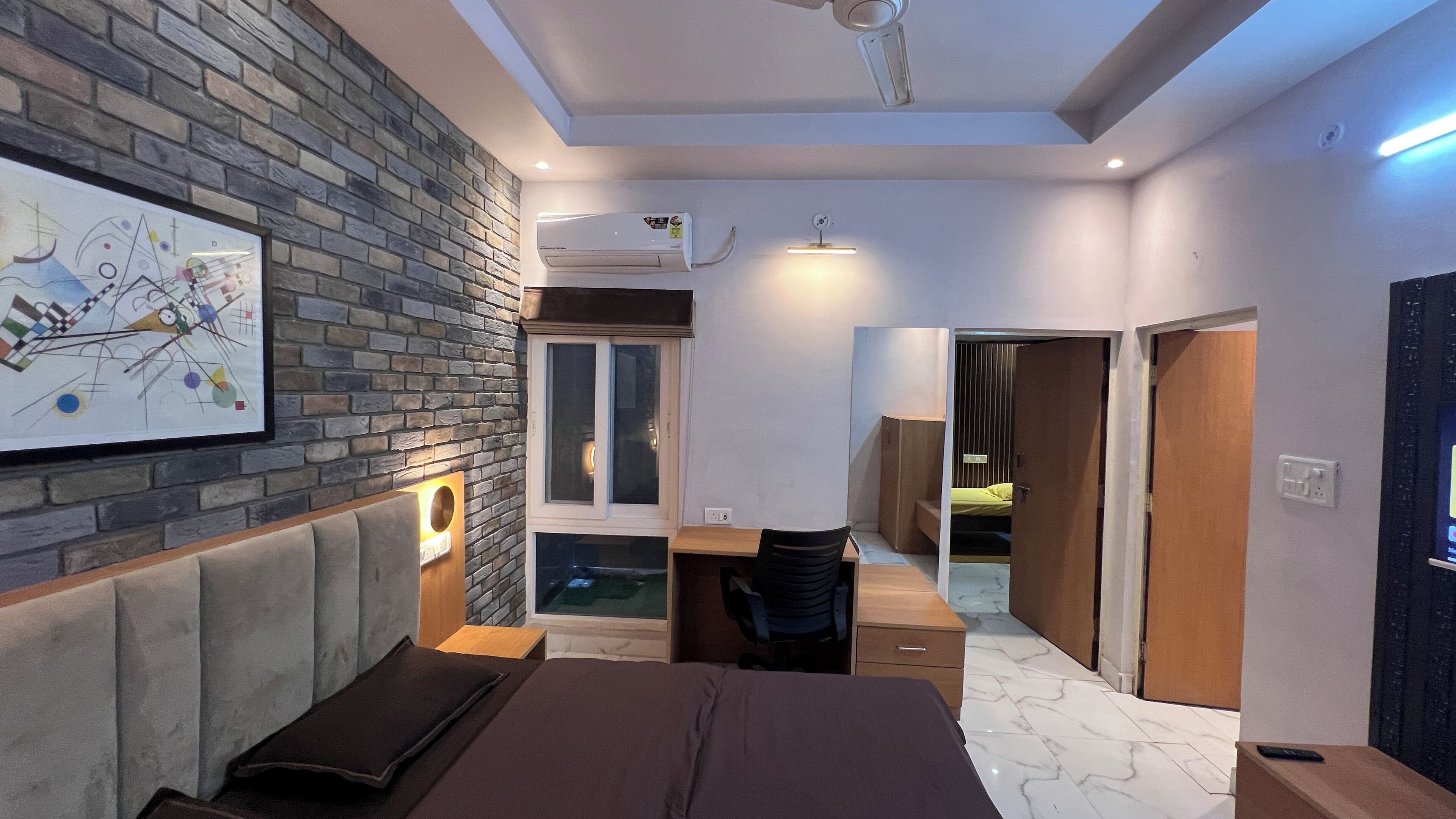 Un dormitorio moderno con pared de ladrillo, una cama, un escritorio y vestidor.