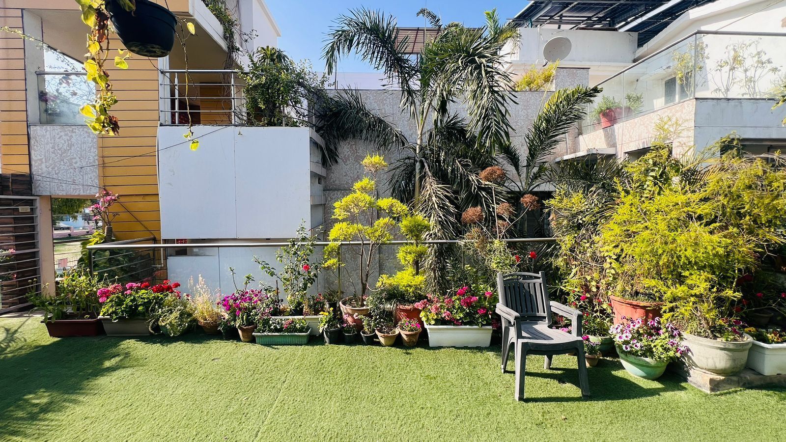 A rooftop garden with various potted plants and a chair.