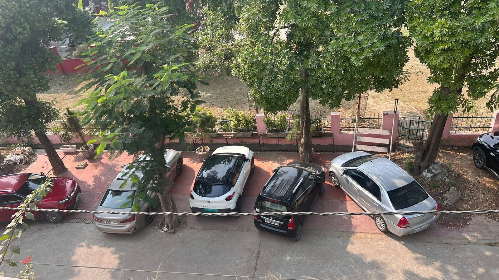 Un aparcamiento con varios coches estacionados bajo árboles.