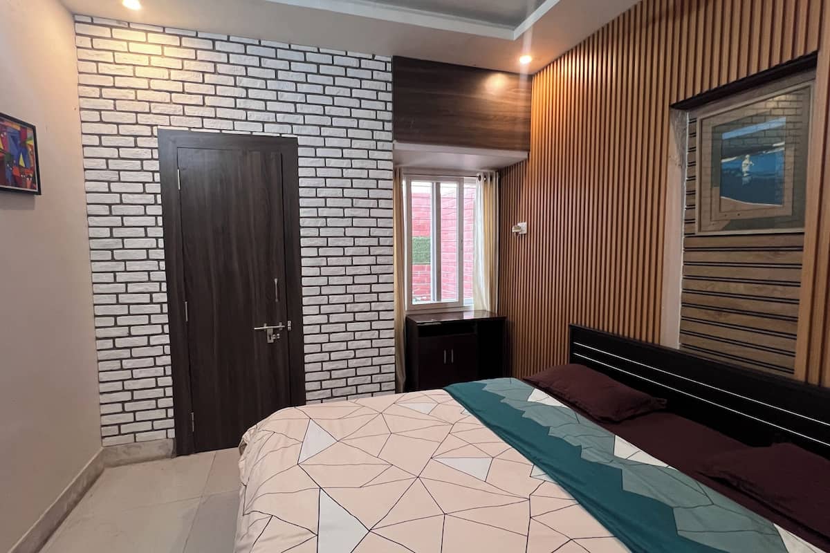 A bedroom with a brick-patterned wall, a wooden headboard, a bed with a geometric-patterned bedspread, and a window with curtains.