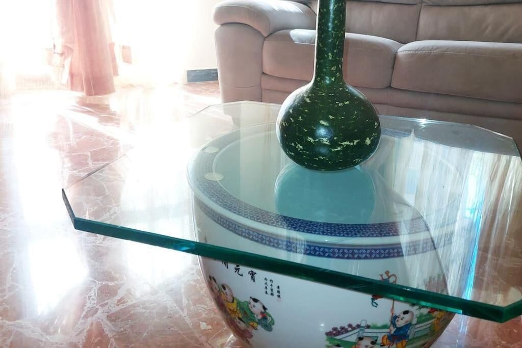 A glass-top table with a decorative vase and a glass shelf.