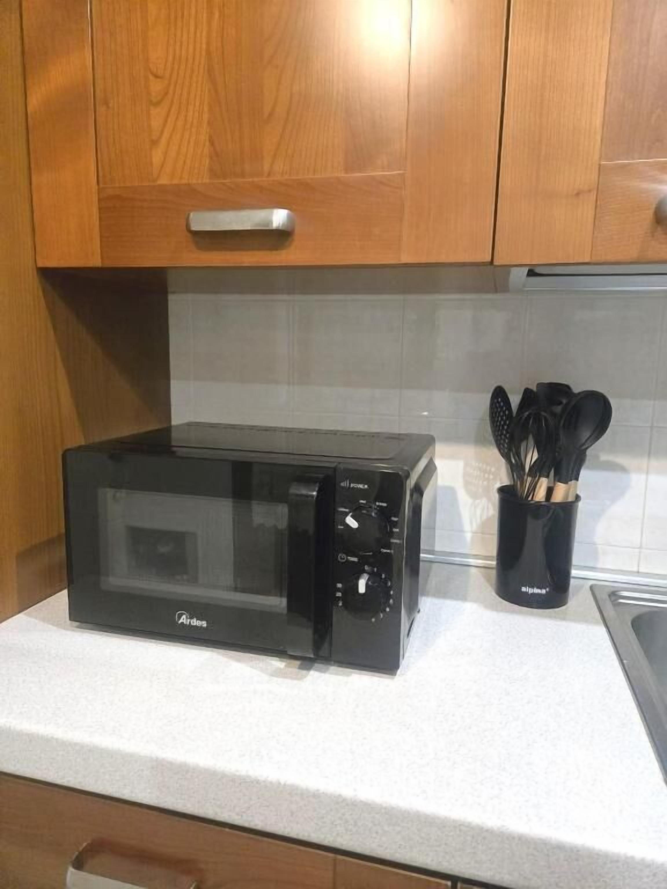 A kitchen with a black microwave oven, wooden cabinets, and a utensil holder on the countertop.