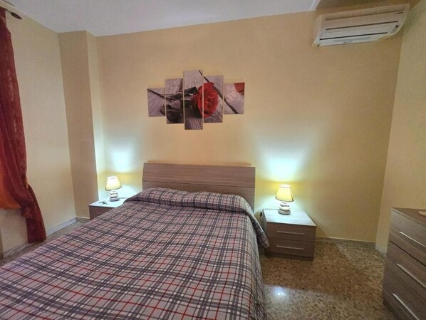 A hotel room with a bed, two bedside tables with lamps, a wall-mounted artwork, and an air conditioning unit.