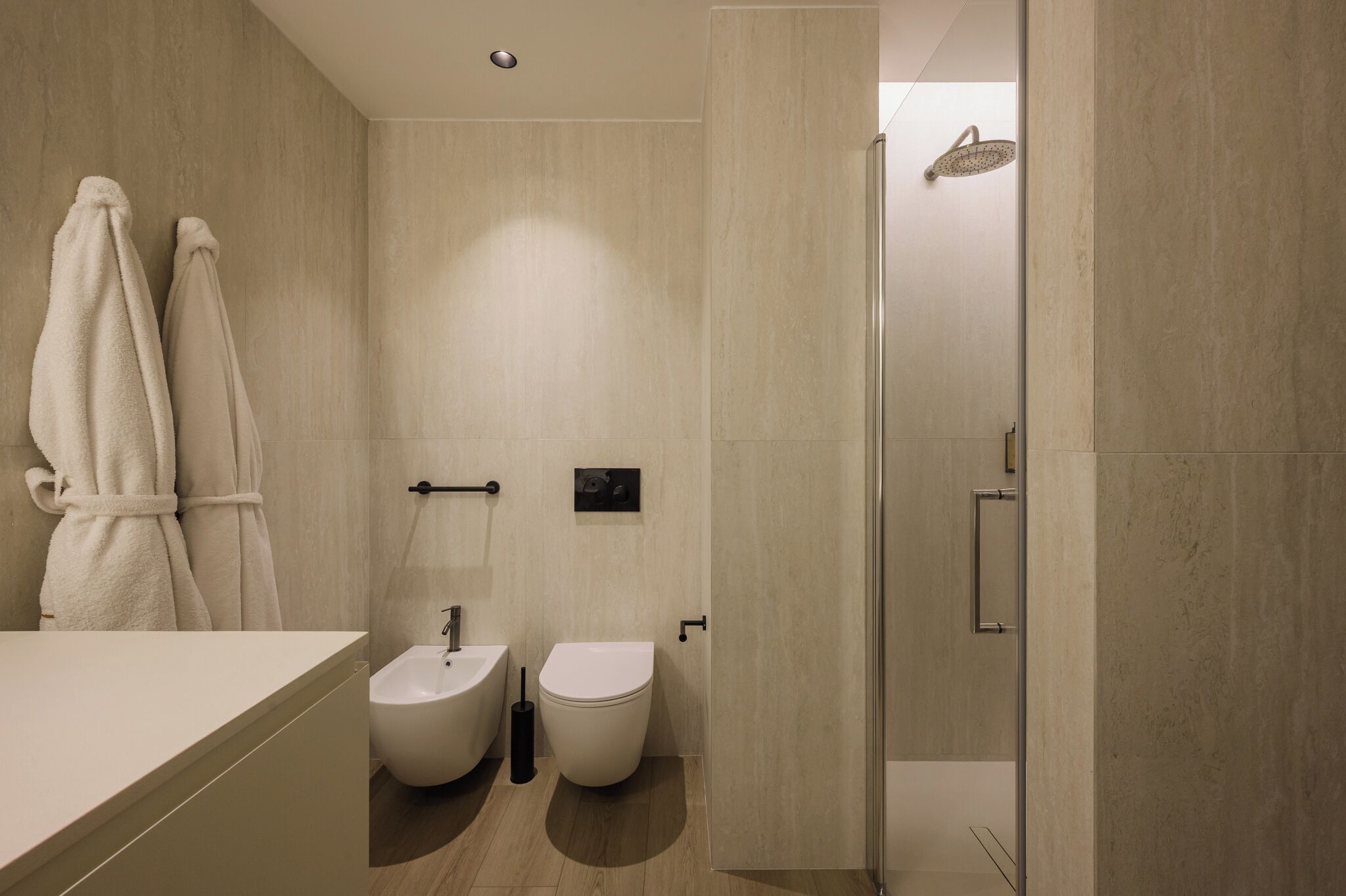 A modern bathroom with a shower, bidet, and a towel rack.