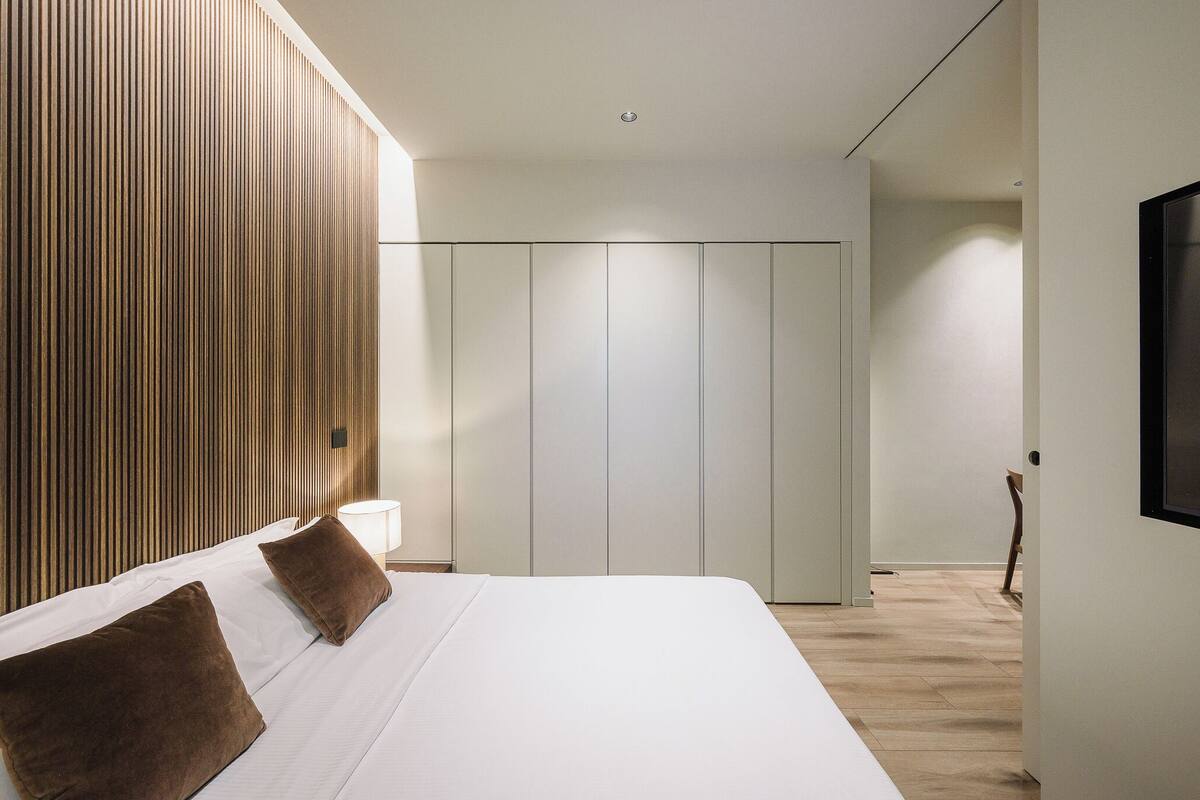 A modern bedroom with a large bed, wooden panel wall, and a wardrobe.
