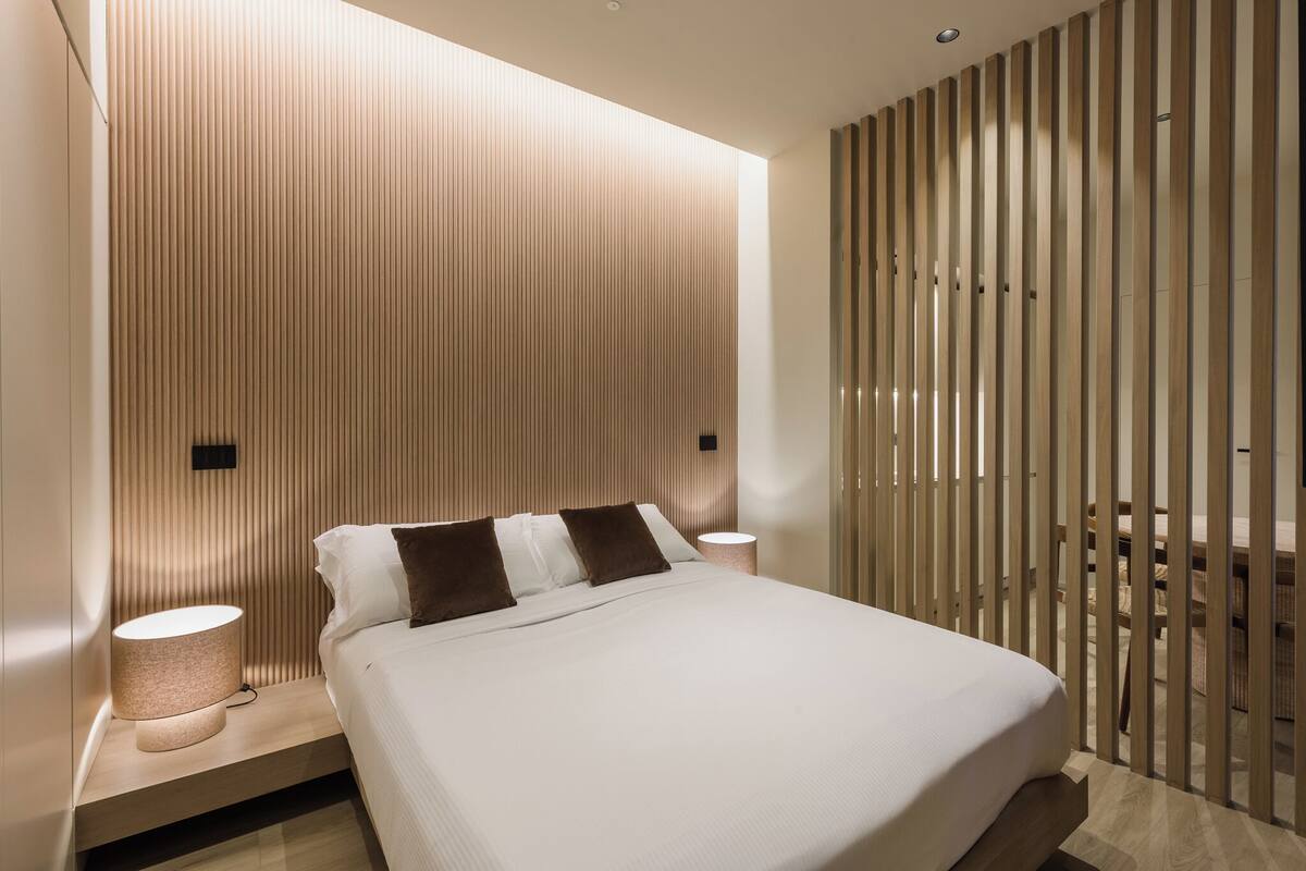 A modern bedroom with a bed, bedside lamps, and a wooden slat partition.