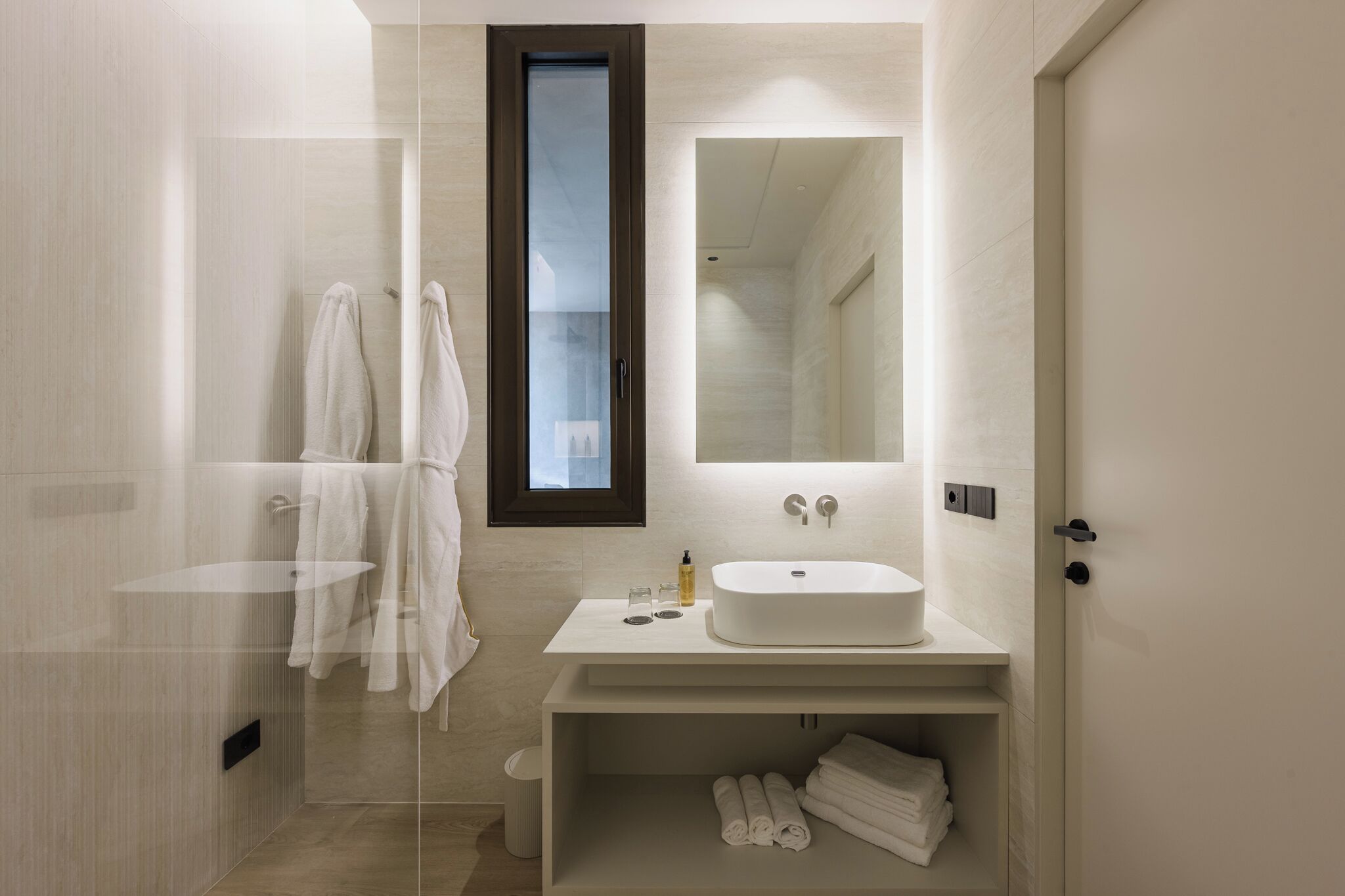 Une salle de bain moderne avec un grand miroir, un lavabo blanc et une douche à parois de verre.