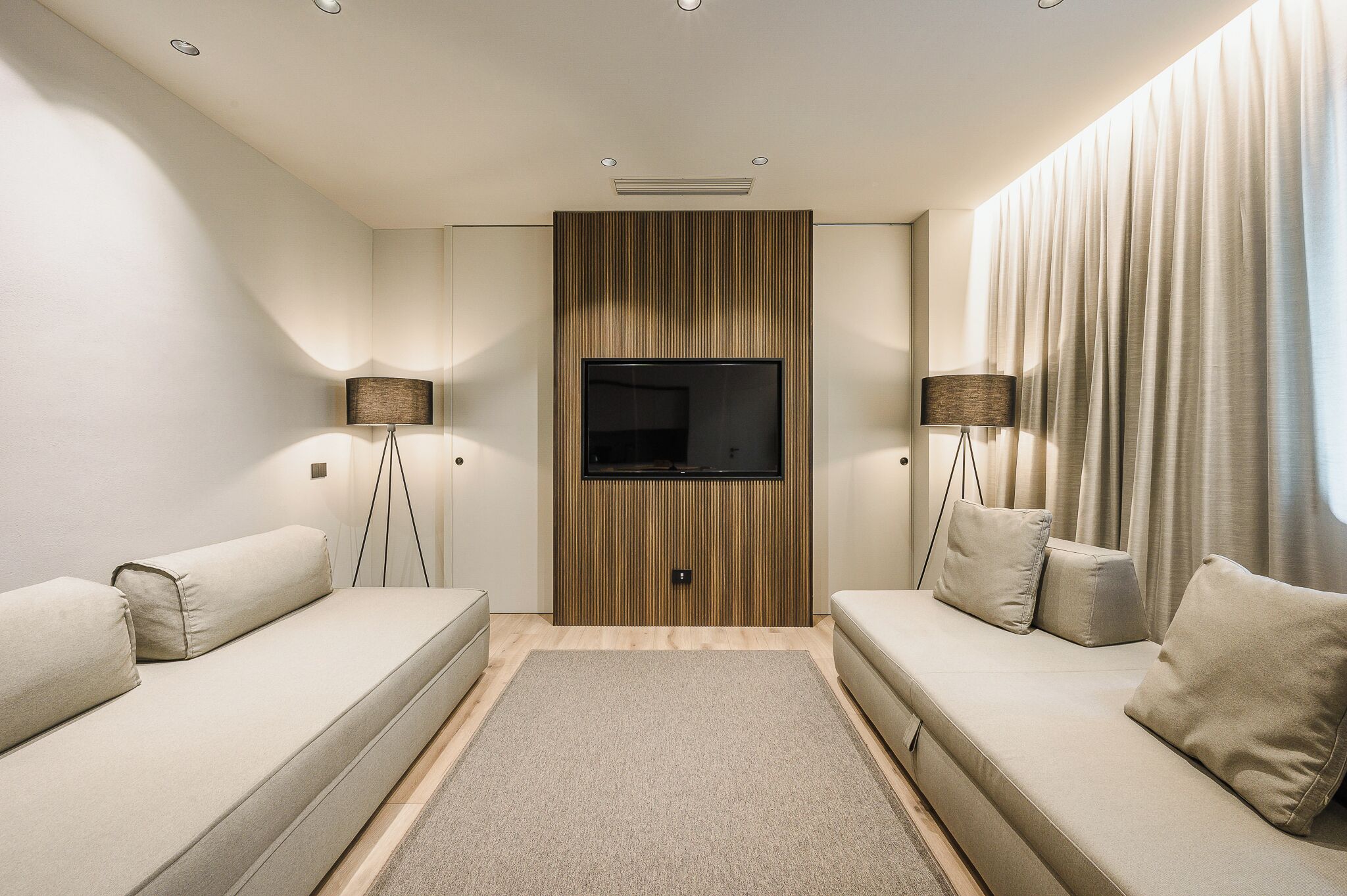 A modern living room with a flat-screen TV, two sofas, and floor lamps.