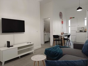 Un salon moderne avec un téléviseur à écran plat, un meuble de rangement blanc, un canapé gris avec des coussins bleus et une petite table ronde.