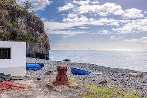 A rocky beach with boats, a red structure, and a cliff. - Sunset Cottage (Madeira)