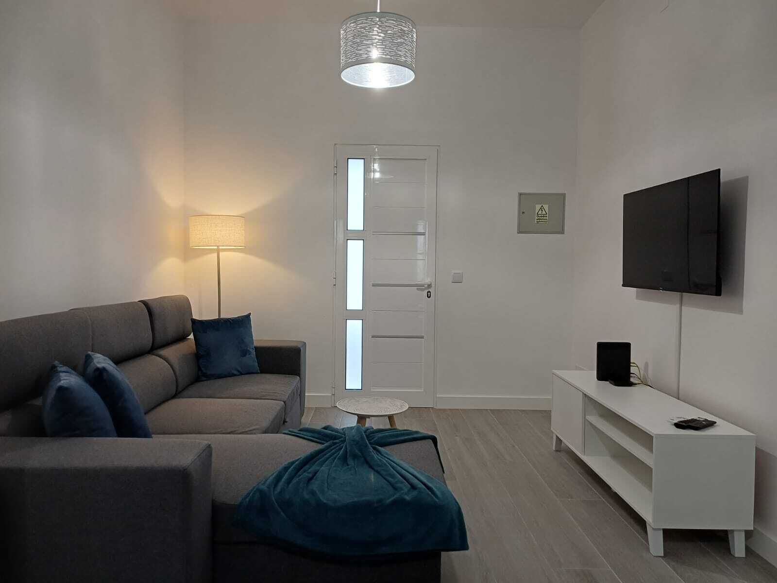 Una sala de estar moderna con un sofá, una mesita redonda pequeña, una lámpara, un televisor y un mueble blanco.