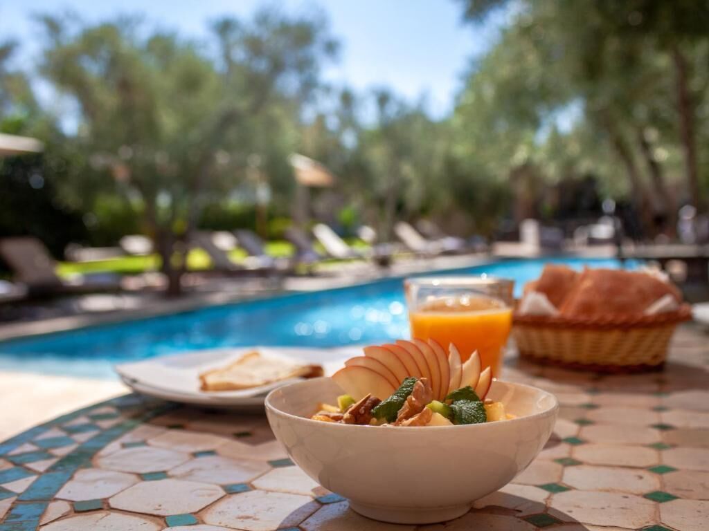 A breakfast setting with a bowl of food, a glass of orange juice, and a basket of bread by a poolside.