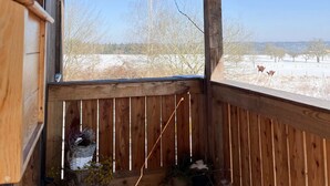 Eine Holzveranda mit Blick auf eine verschneite Landschaft und kahle Bäume.
