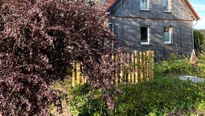 Ein rustikales Holzhaus mit rotem Dach, umgeben von üppigem Grün und blühenden Bäumen.