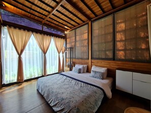 Quarto com cama grande, teto de madeira e vista pela janela.