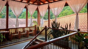 A covered outdoor seating area with wooden furniture and a view of greenery. - Lake Reach Hotel (Kandy)