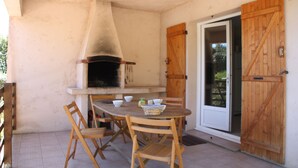 An outdoor patio with a round wooden table, four wooden chairs, a pizza oven, and a sliding glass door. - Gite Casteddu 2 with heated pool for lovers of peace and nature (San Gavino di Carbini)