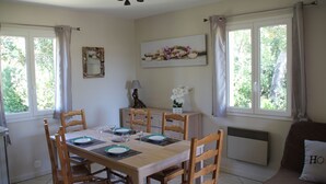 A dining room with a wooden table set for four, surrounded by chairs. There is a window with curtains, a radiator, and a wall-mounted shelf with decorative items. - Gite Casteddu 2 with heated pool for lovers of peace and nature (San Gavino di Carbini)