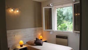 A bedroom with a single bed, two bedside lamps, a window with curtains, and a view of greenery outside. - Gite Casteddu 2 with heated pool for lovers of peace and nature (San Gavino di Carbini)