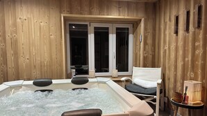 Ett spa-rum i trä med ett bubbelbad, ett fönster och en stol.