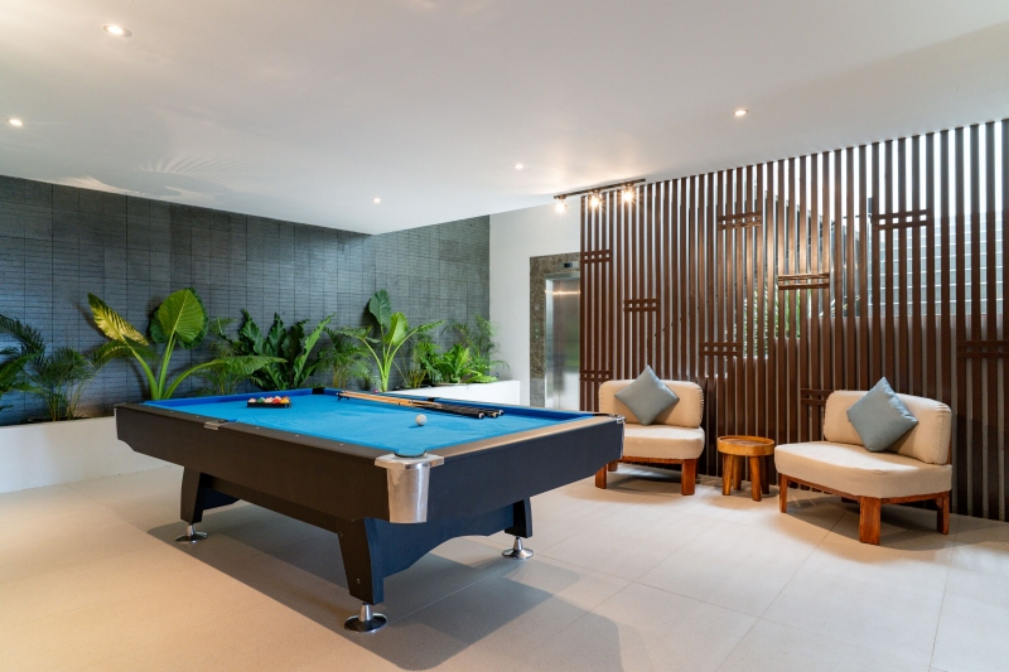 A pool table in a modern room with a seating area and plants.