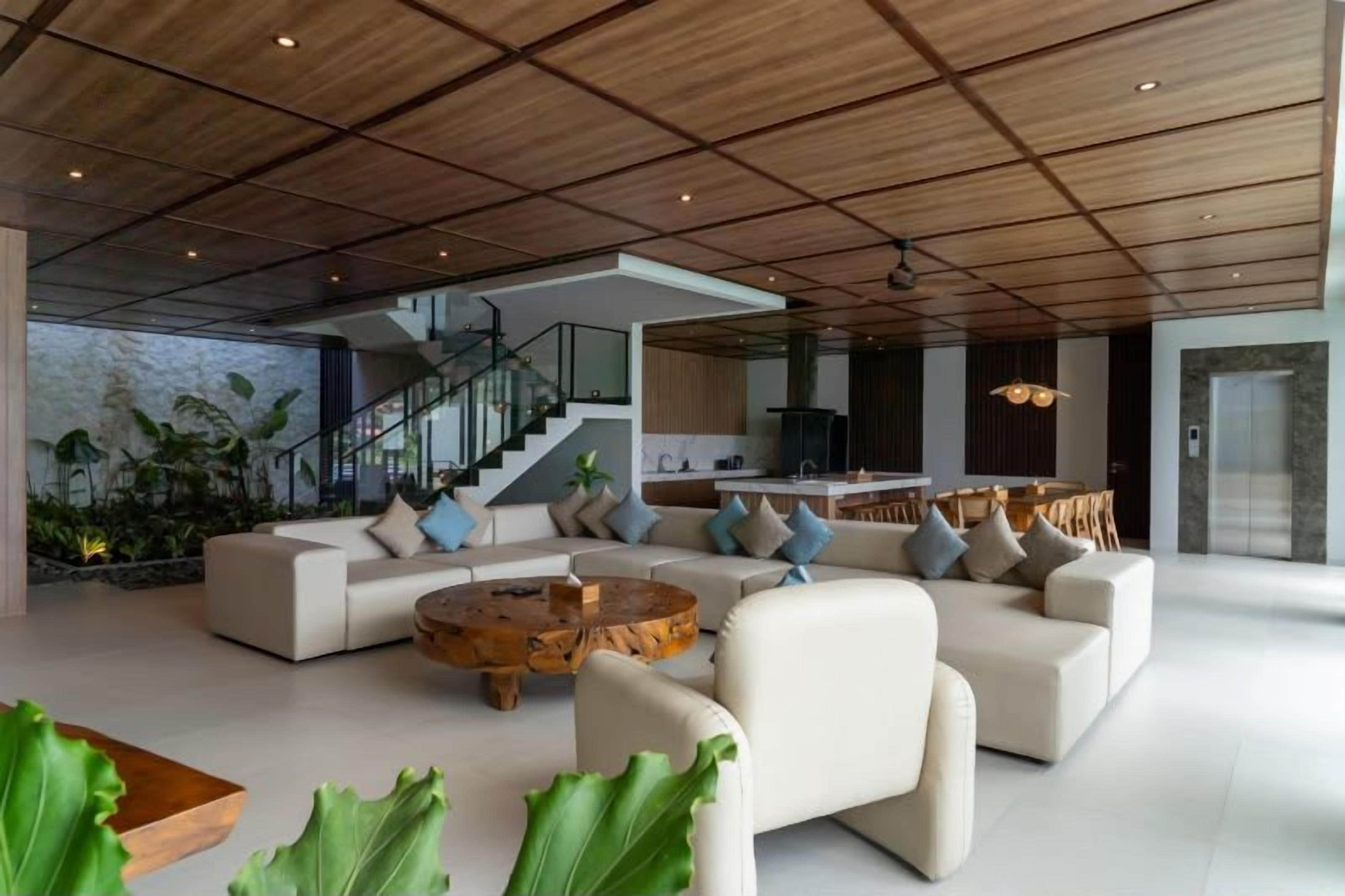 Un área de estar amplia con diseño moderno, que incluye un sofá grande, una mesa de centro de madera y una escalera que conduce a un nivel superior.