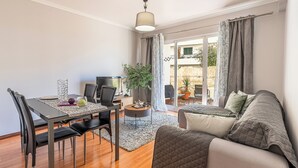 Ein modernes Wohnzimmer mit Essbereich, einer Couch, einem Fernseher und einem Balkon mit Vorhängen.